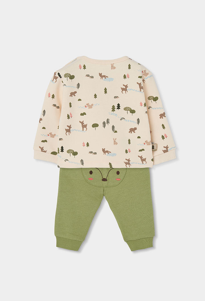 A two-piece baby clothing set featuring a cream-colored long-sleeve top with a woodland animal print (deer, foxes, trees) and sage green pants with a fox face applique on the front.